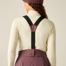 A view of the back of a person wearing beige long sleeves and purple trousers with black suspenders.
