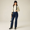 Model wearing navy D2B Effused III pants with black suspenders and a cream zippered top, holding a trekking pole.