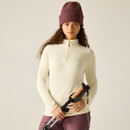 A woman in a cream zipped long-sleeve top and maroon beanie holds trekking poles against a neutral background.