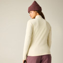 A woman wearing a cream long-sleeve top with a high collar, paired with a purple knitted beanie.