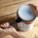 A person using a Dekton painters pry bar to open a paint can.