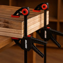 Two Dekton clamps holding stacks of wooden boards on a workbench.