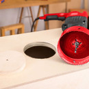 A holesaw kit with a red saw and a large cut-out piece of wood on a work surface.