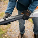Close-up of gloved hands connecting the black blower tube to a STIHL cordless leaf blower.