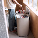 A person holding red-handled laundry bags over a cream-coloured, oval-shaped laundry basket with a lid, filled with clothes.