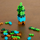 A small 3D structure made of colourful interlocking plastic pieces resembling a snake plant, set against a brown surface with loose pieces nearby.