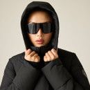 A woman in a black puffer jacket with a hood and oversized black sunglasses, standing against a light background.