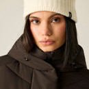 A close-up of a woman wearing a brown puffer jacket with a high collar and a cream knitted beanie.