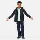 A smiling boy stands with arms outstretched. He's wearing a black jacket, light teal shirt, dark pants, and sneakers, exuding a confident and casual vibe.