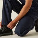 Close-up of navy work trousers at ankle, worker adjusting hem over black safety boots, durable industrial cargo pants