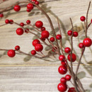 Close-up of decorative red berry garland featuring vibrant glossy berries and natural-look branching stems for seasonal displays and wreaths.