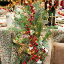 Christmas table centrepiece decorated with red berry garland, evergreen foliage, eucalyptus leaves and warm fairy lights for festive home décor.