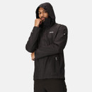 Man in a black hooded jacket stands thoughtfully with his hand on his chin against a plain background, conveying a sense of contemplation.