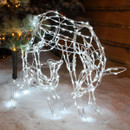 Illuminated LED deer Christmas decoration with a wireframe design and cool white lights, displayed on artificial snow beside a decorated tree for festive indoor décor.