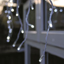 Close-up of white LED snowing icicle lights hanging from a roof edge, featuring a cascading snowfall effect for festive outdoor lighting.