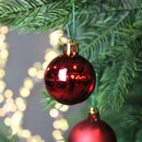 Glossy red Christmas bauble ornament hanging on a Christmas tree branch, reflecting festive lights and seasonal décor.