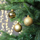 Gold Christmas baubles hanging on a fir tree, featuring glossy, matte and glitter finishes with warm white fairy lights in the background.
