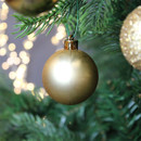 Matte gold Christmas tree bauble suspended from a fir branch, creating a classic and sophisticated festive display.