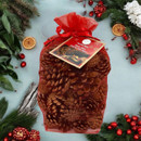 Bag of scented pine cones with festive red organza gift packaging, displayed among Christmas greenery, berries and seasonal decorations for home fragrance and décor.