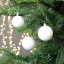White Christmas baubles hanging on a fir tree, featuring glossy iridescent and textured finishes with warm white fairy lights in the background.