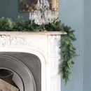 Artificial pine Christmas garland draped over an ornate fireplace mantel, creating a classic festive display with lush green foliage and seasonal décor.