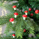 Small red mushroom decorations attached to Christmas tree branches.