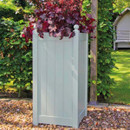 Tall sage green wooden planter with vertical panel sides, filled with trailing red and purple foliage, on gravel in a garden.