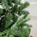 Close-up of an artificial green Christmas tree branch against a white wall.