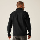 Back view of black fleece jacket showcasing clean design, high collar, and relaxed fit, paired with grey denim jeans for a modern casual look