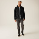 Full body shot of male model in black zip-up fleece jacket layered over a white t-shirt, styled with grey jeans and black sneakers for a smart casual outfit
