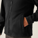 Close-up of black fleece jacket showing full-length front zipper and soft brushed fabric texture, with hand in side pocket highlighting functional design and comfort