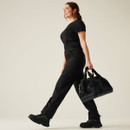 Side profile of women’s black cargo work trousers with functional pockets and reinforced fabric, styled with safety boots and a portable tool kit.