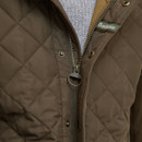 Close-up of a brown quilted jacket with a visible Barbour logo on the zipper tab. Layered over a light grey knit jumper, conveying warmth and casual style.