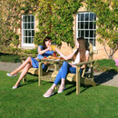 Two women relaxing in a wooden companion chair set with a central table, enjoying drinks in a garden.