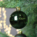Glossy dark green Christmas bauble hanging on an evergreen branch, reflecting warm festive lights for a classic holiday look.
