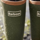 Close-up of Barbour logo on green rubber wellington boots with water droplets on the surface.