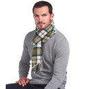 A person with short hair sits wearing a grey jumper and a green plaid scarf. The expression is calm, and they are seated against a white background.