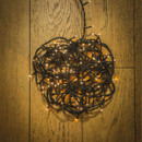 Coiled antique white LED string lights with green cable displayed on a wooden floor, showing compact storage and warm glowing bulbs.