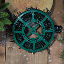 Christmas LED string lights wound on a green storage reel, displayed on a rustic wooden surface with artificial snow and festive greenery, ready for seasonal decorating and easy storage.