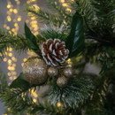 Close-up of a Christmas tree branch with a pinecone, glittery gold ornaments, and green leaves, set against warm, blurred festive lights. Cosy holiday vibe.