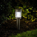 Stainless steel solar-powered garden stake light glowing in a flower bed at night.