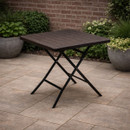 A square, folding table with a slatted dark brown tabletop and black metal legs positioned on a patio.