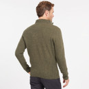 Man in olive green jumper with a high collar, facing away. He has short brown hair and wears dark pants. Background is plain white, evoking simplicity.