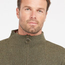 A man with short hair and a beard wears a textured, olive green zip-up jumper. The background is plain white, creating a neutral, calm tone.