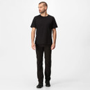 A man with a short beard stands looking left, wearing a black t-shirt and pants, against a plain white background. The tone is neutral and casual.