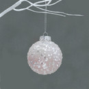 A close up view of a blush pink ombre, sequinned bauble hanging from a white branch against a grey background.