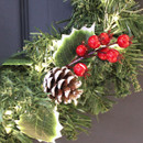 A close up view of a foliage pick with red berries and three brown pinecones, amongst a green garland.