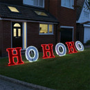 Illuminated HO HO HO outdoor Christmas sign displayed on a front lawn, featuring alternating red and white LED tinsel letters for a festive garden decoration.