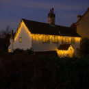 The NOMA 960 Snowing Icicle LED Lights Warm White - 20.6m hanging on a house
