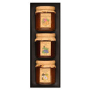 Three glass jars neatly arranged in a black presentation box, each with rustic brown paper lids and illustrated labels showing Apricot and Passionfruit Jam, Blackcurrant Jam, and Pink Grapefruit and Mandarin Marmalade.